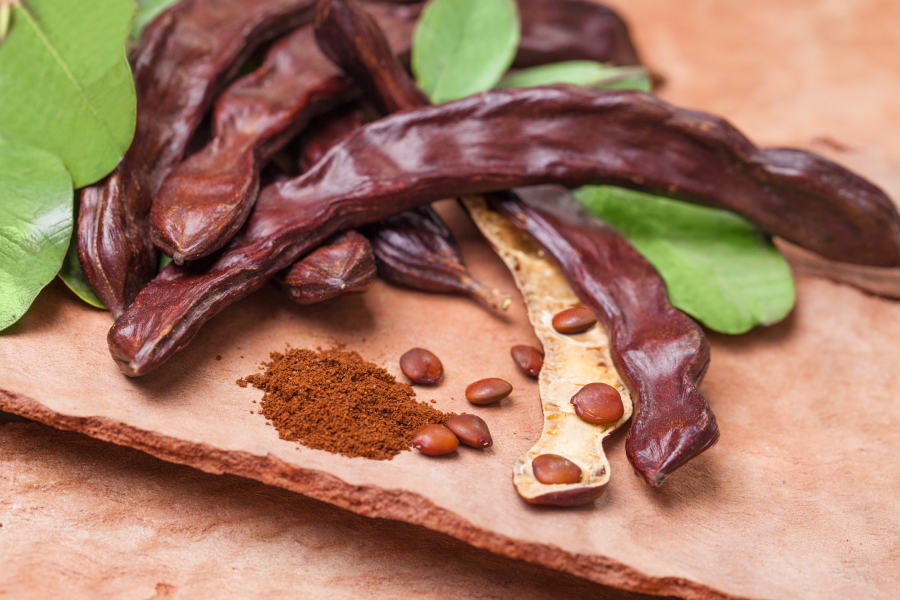 Carob pods and powder displayed on a clay surface with green leaves